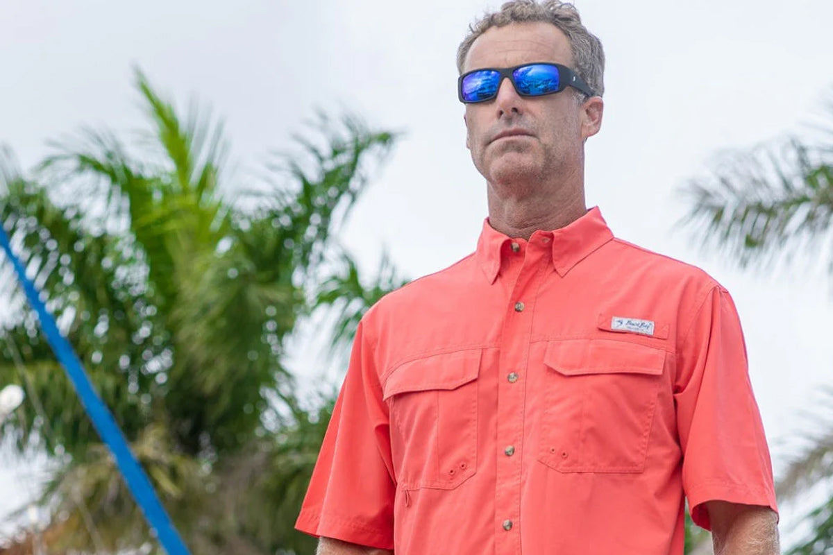 Man wearing a red shirt with a logo, sunglasses, and a blue pole in the background